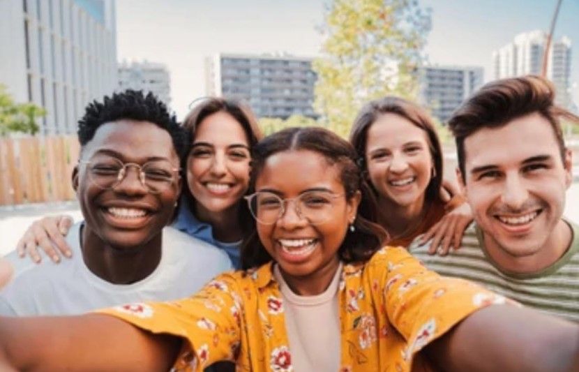 Five smiling young adults taking a selfie together outdoors